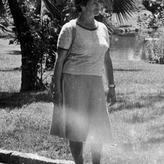 Woman stands near a park with palm trees.