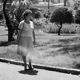 Woman stands near a park with palm trees.