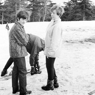 Here's a brief summary of the image: Two people in snowy landscape; one appears to be struggling.