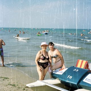 Two women stand beside a boat on a sandy beach.