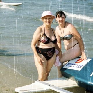 Two women stand beside a boat on a sandy beach.