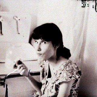 Woman in kitchen, holding a glass with a liquid.