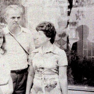 Man stands between two girls in front of a building.