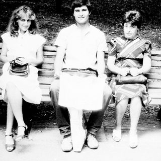 Three people sit on a park bench in black and white.