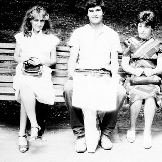 Three people sit on a park bench in black and white.