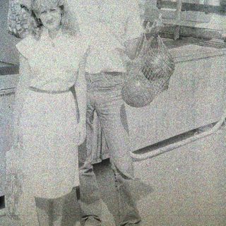 Here's a brief summary of the image: Couple stands near a freezer, holding a bag of something.