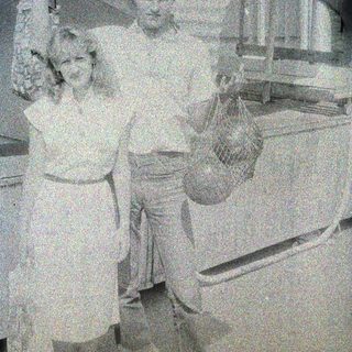 Here's a brief summary of the image: Couple stands near a freezer, holding a bag of something.