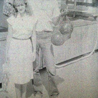Here's a brief summary of the image: Couple stands near a freezer, holding a bag of something.