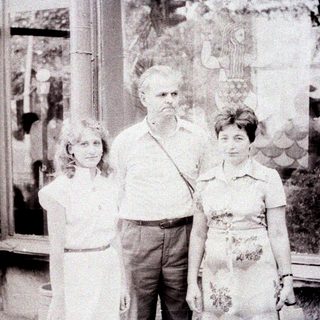 Three people pose near a stained glass window.