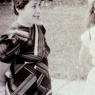 Two smiling women standing outdoors in a grassy area.