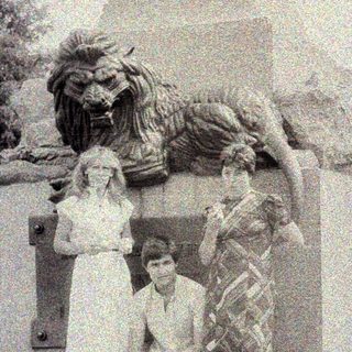 Here's a brief summary of the image: Two people pose near a statue and stone monument.