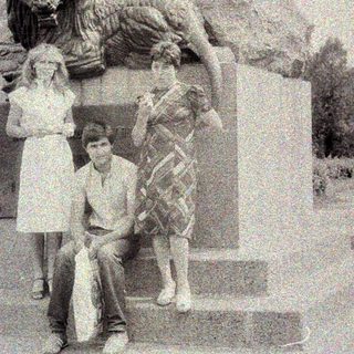 Here's a brief summary of the image: Two people pose near a statue and stone monument.