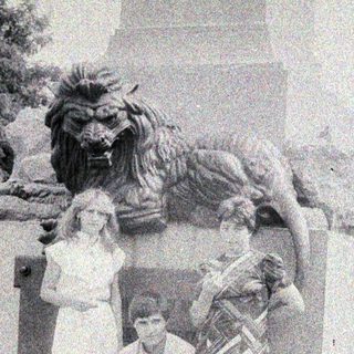 Three people pose near a stone lion statue.