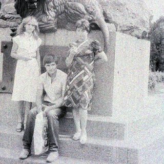 Three people pose near a stone lion statue.