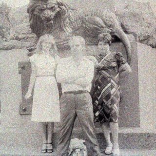 Three people pose near a statue with a lion.