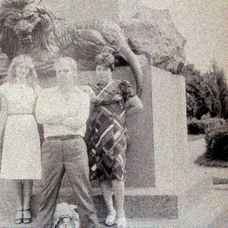 Three people pose near a statue with a lion.