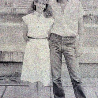 Here's a brief summary of the image: Couple posing outdoors in front of a building.