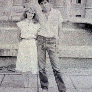 Here's a brief summary of the image: Couple posing outdoors in front of a building.