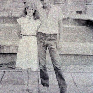 Here's a brief summary of the image: Couple posing outdoors in front of a building.