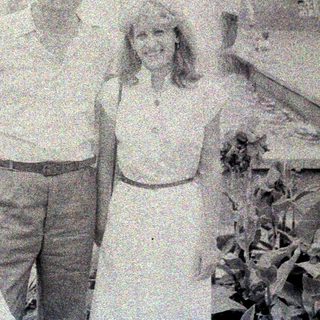Couple poses in front of a building with a fountain.