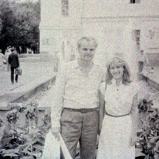 Couple poses in front of a building with a fountain.