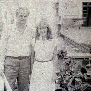 Couple poses in front of a building with a fountain.