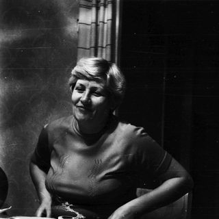 Here's a brief summary of the image: Woman seated at a table, smiling, in a vintage setting.