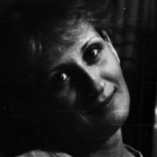 Woman seated near a television, in a darkened room.