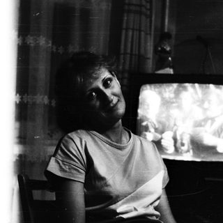 Woman seated near a television, in a darkened room.