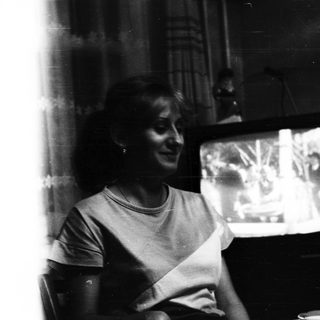 Woman seated, watching television in a dimly lit room.