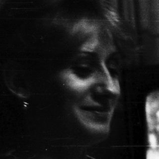 Woman seated, watching television in a dimly lit room.