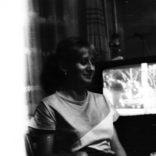 Woman seated, watching television in a dimly lit room.
