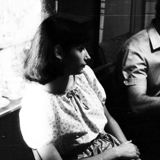 Here's a brief summary of the image: Black and white photo of a family gathered around a table.