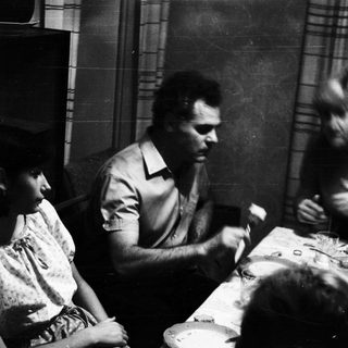 Here's a brief summary of the image: Black and white photo of a family gathered around a table.