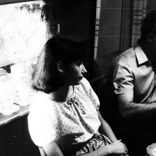 Here's a brief summary of the image: Black and white photo of a family gathered around a table.