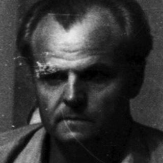 Here's a brief summary of the image: Two men seated, looking down, against a patterned wall.