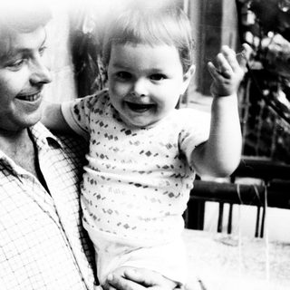 Man holds smiling baby on his lap outdoors.