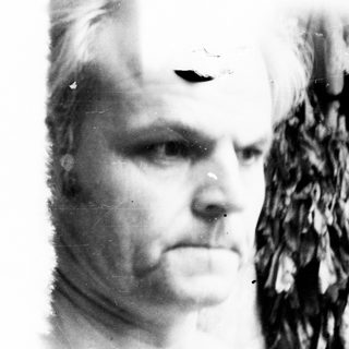 Man's portrait with feathered headdress, appearing aged and weathered.