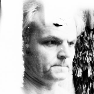 Man's portrait with feathered headdress, appearing aged and weathered.