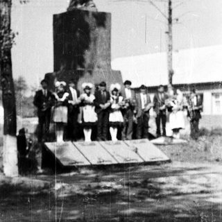 Group poses near a statue in a rural setting.