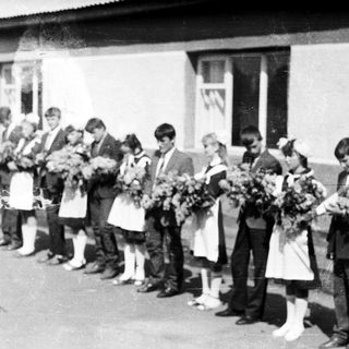Group of children in formal wear stand outside a building.