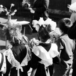 Children in aprons observe an event outdoors.