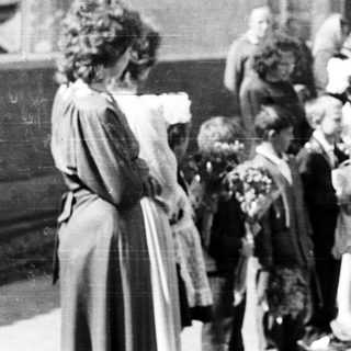 Group of children with flowers standing outside a building.