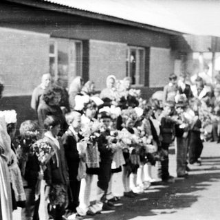Group of children with flowers standing outside a building.