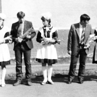 Group of people in vintage clothing stand outdoors.