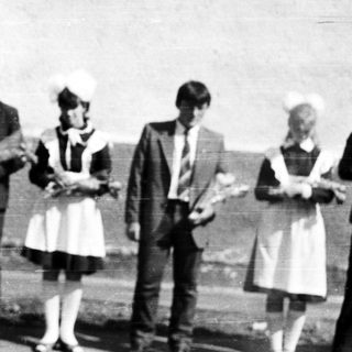 Group of people in vintage attire stand outside a building.