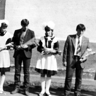 Group of people in vintage attire stand outside a building.