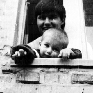 Here's a brief summary of the image: Person and baby peering out of a window.