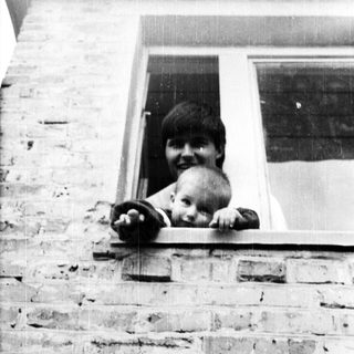 Here's a brief summary of the image: Person and baby peering out of a window.