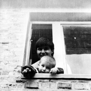 Here's a brief summary of the image: Person and baby peering out of a window.